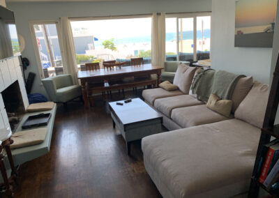 inside living room at a beach house with a comfy L shaped sofa and dining table and ocean view with hardwood floors